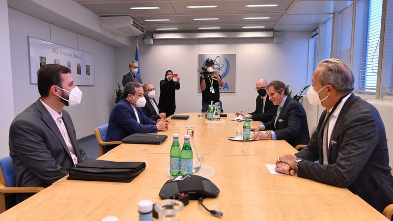 Abbas Araghchi in a blue suit and mask seated at a conference table opposite IAEA Director General Rafael Grossi
