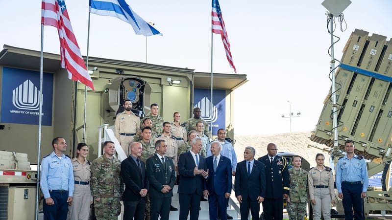 Iron Beam laser beam director on a shelter beside an Iron Dome launcher, with officials and soldiers in front