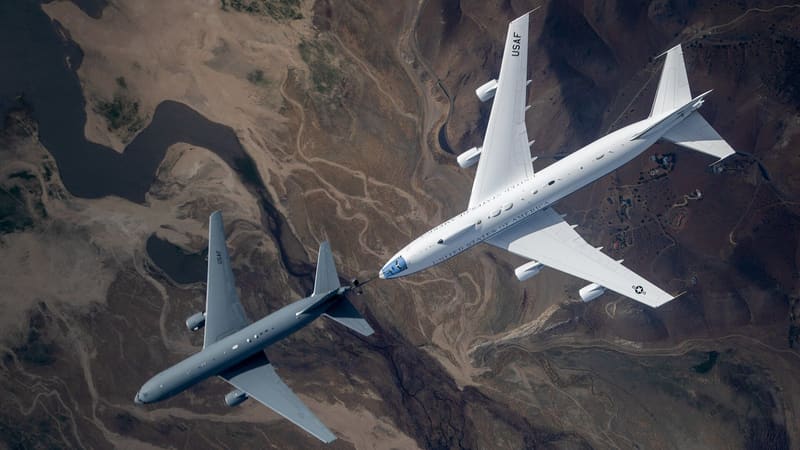 E-4B Nightwatch refueling from a gray KC-46 tanker's boom, seen from above over arid hills