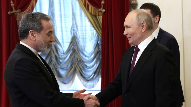 Abbas Araghchi shaking hands with Vladimir Putin in front of red curtains