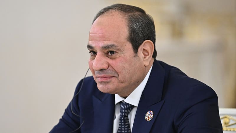 Abdel Fattah el-Sisi, smiling slightly, with an interpretation earpiece and summit lapel pin at a microphone