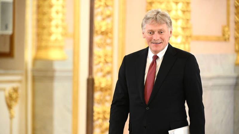 Smiling Kremlin spokesman Dmitry Peskov in a dark suit and red tie, walking through a gilded hall