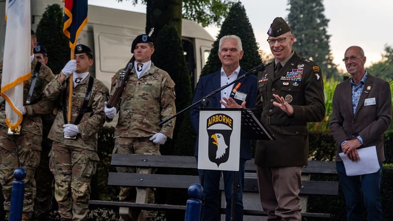 Maj. Gen. Brett Sylvia in Army dress uniform speaks at a lectern with a 101st Airborne sign outdoors