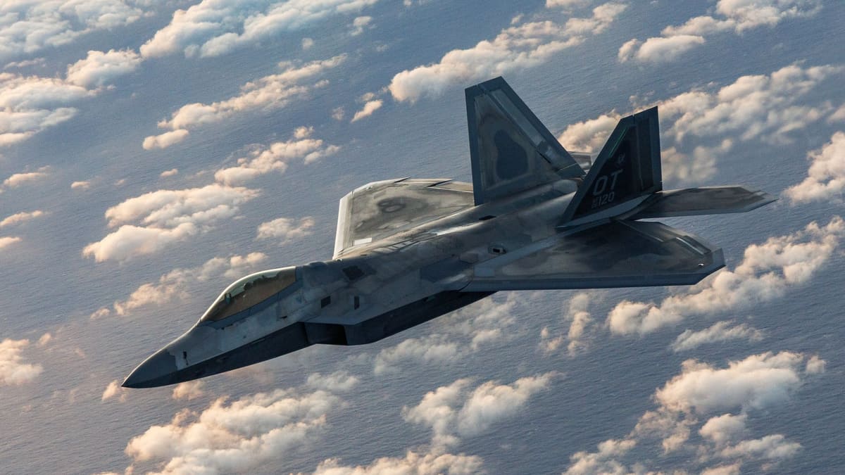 An F-22 Raptor stealth fighter banks over a layer of scattered white clouds above the sea