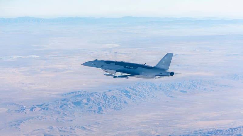 A grey YFQ-44A Fury drone with U.S. Air Force markings flies above the brown Mojave Desert and distant mountains