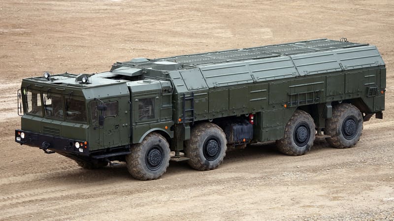 A green eight-wheeled Iskander-M missile launcher truck with its roof closed on a dirt demonstration ground